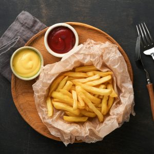 French fries. Tasty French fries server on parchment paper on wooden cutting board with tomato and c